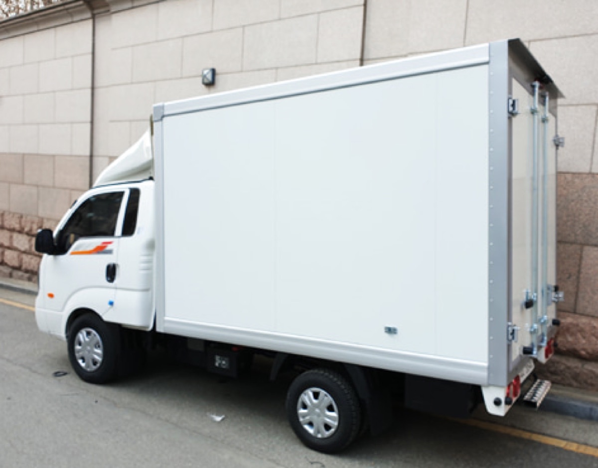 A light dry-van box truck parked on a street, its cargo body made of large flat panels