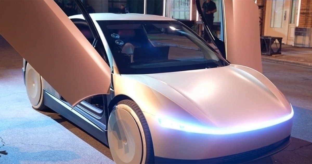A prototype electric passenger car with matte body panels and an illuminated front light bar, doors open
