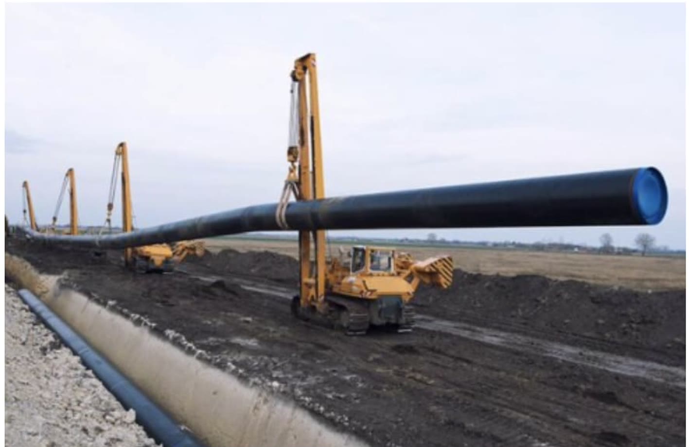A pipeline section being lowered into a trench by side-boom tractors
