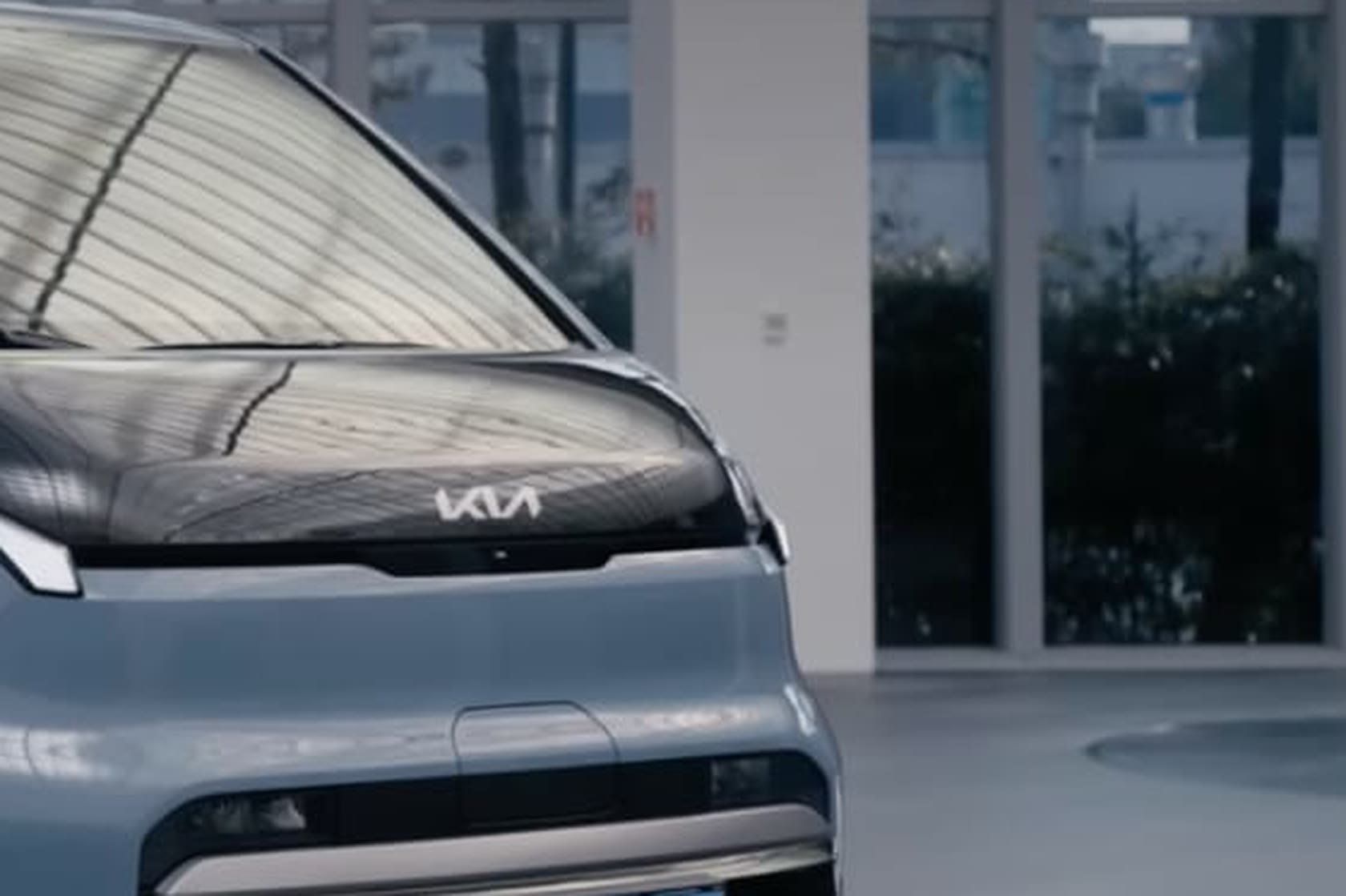 The high-gloss black bonnet of a Kia PV5, reflecting a glazed façade, with no painted finish